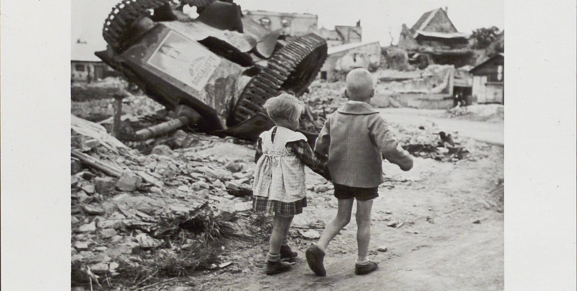 Deux enfants passent devant un char renversé dans un village en ruines, Ammerschwihr (France), 1944-1945, photographie de Thérèse Bonney.