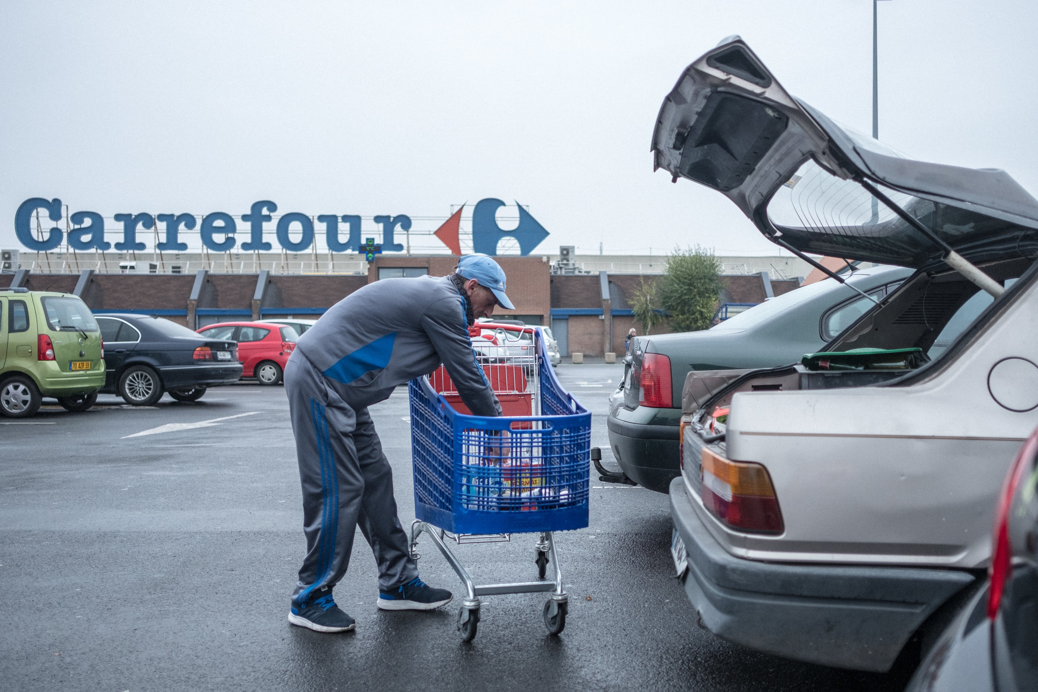 Denain (59), octobre 2017. Guillaume charge le coffre de sa vieille 309 sur le parking de Carrefour. L'hypermarché a la particularité d'être situé en plein centre-ville.